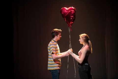 Two actors hold red heart balloons