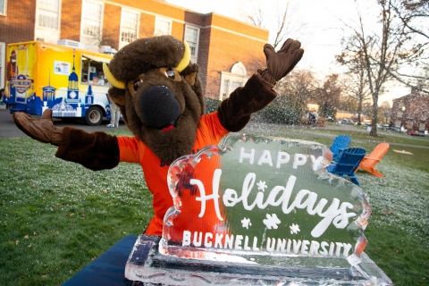 Bucky the Bison mascot extends his arms as he stands behind an ice sculpture that says "Happy holidays, Bucknell University"