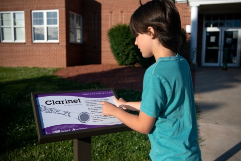 Child reading a poem titled &#039;Clarinet&#039; on the Linntown Poetry Path.