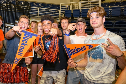 A group of students in Bucknell gear hold Class of 2026 pennants, signs and streamers while smiling at orientation