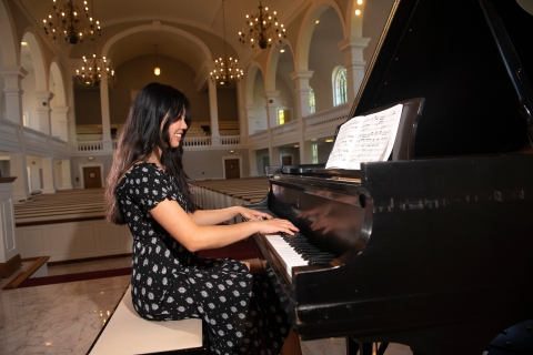 Vivian Kuang sits at a black grand piano in a black floral dress.