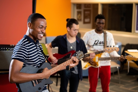 Three students playing their guitars