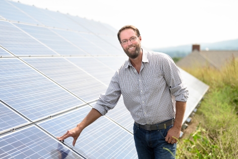Nate Siegel stands and smiles with an array of solar panels