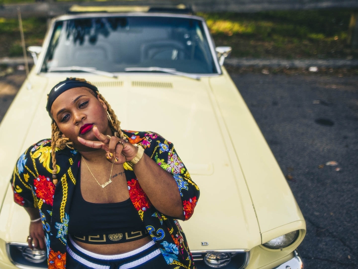 Oompa Williams &#039;14 leans on the hood of a yellow mustang showing a peace sign.