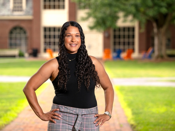 Jasmine Jones &#039;25 stands on campus on a brick walkway with green grass on both sides of it, with her hands on her hips and smiling.