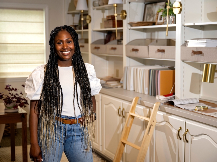 Chrissy Haney Scheimreif ’16 wears a white shirt and jeans and stands in her home office/studio while smiling.