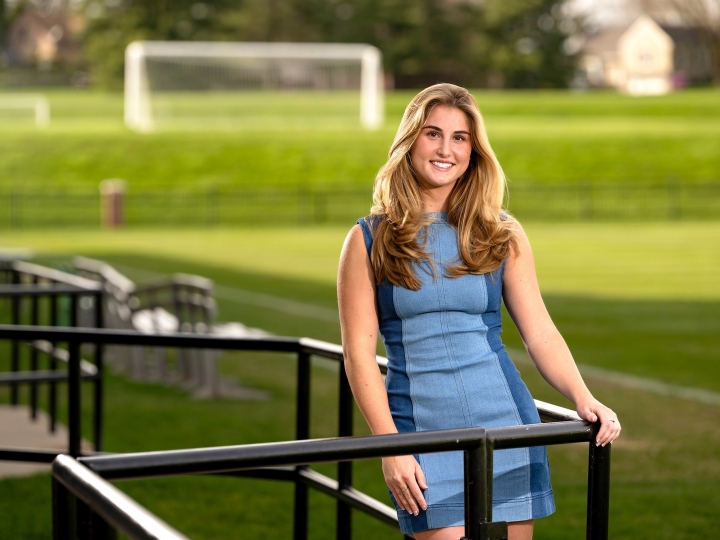 Lea Tarzy &#039;24 poses in a blue dress in the stands of a soccer field.