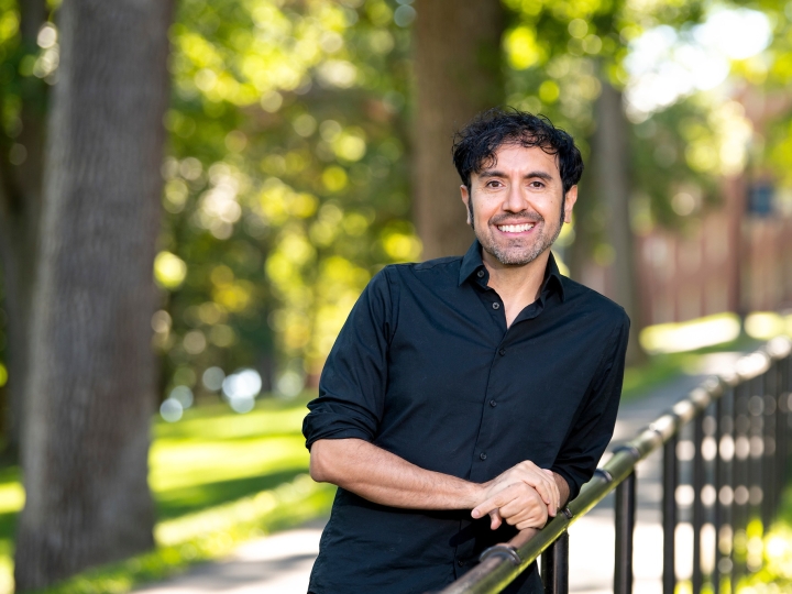 Portrait of Eddy Lopez leaning on a railing outdoors in a wooded area.