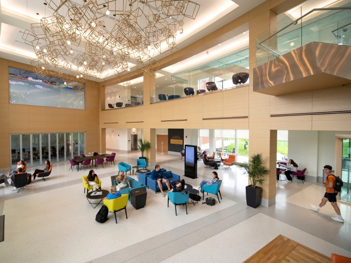 A down angle photograph of students walking and sitting in the lobby of Holmes Hall.