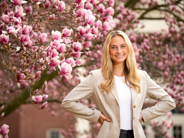 Abigail Kates &#039;24 stands with her hands on her hips and smiles, cherry blossoms are in the background