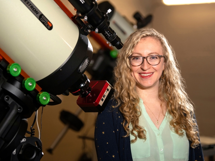 Professor Jackie Villadsen stands next to a large telescope on Bucknell&#039;s campus and smiles.