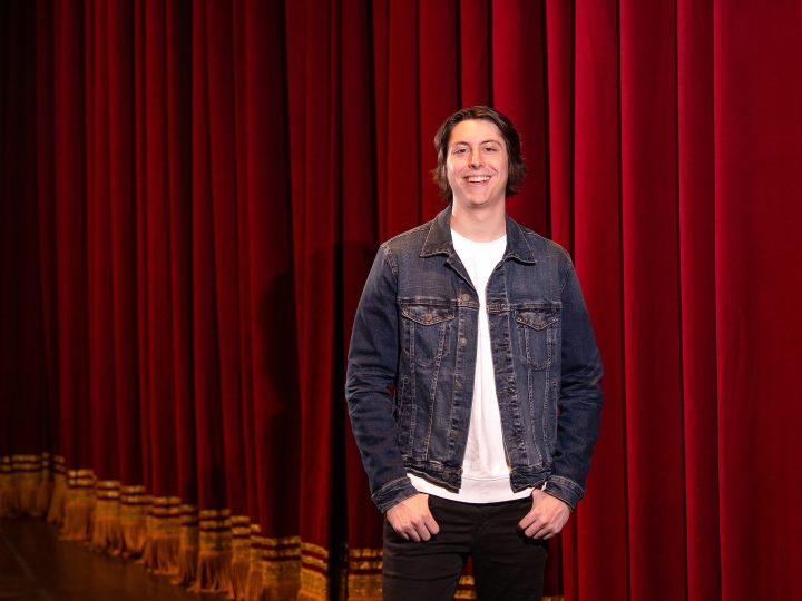 Reid Fournier stands on a stage, a red stage curtain is in the background.