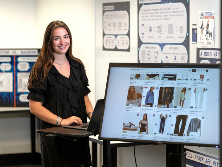 Ava Sklar smiles beside a monitor displaying clothing listings on her Bucknell Refit website.