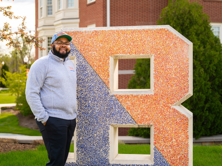 Jawaad "KJ" Benson stands next to a large letter B that is part blue and part orange.