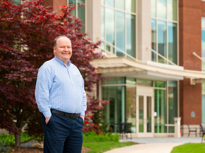 Joe Wilck stands with his hands in his pockets and smiles outside of Holmes Hall.