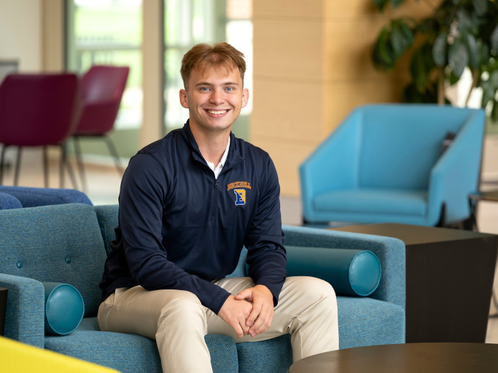 Kaleb Eger sits on a teal chair and smiles.