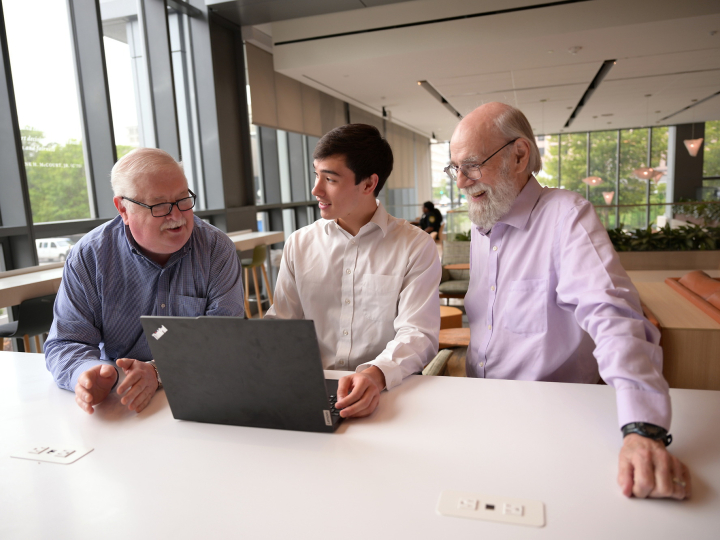 Max Quan is working on a laptop in an office setting with David Hamill to his right and Jack Hoadley to his left.