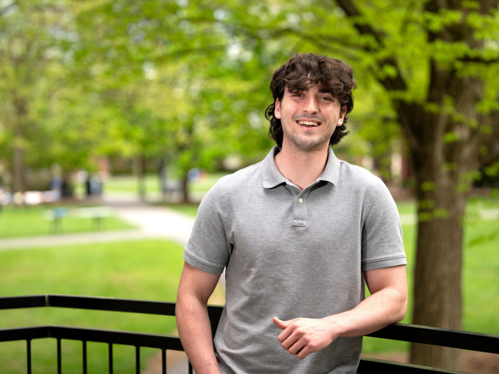 Michael Evanick stands outdoors on campus and smiles; green grass and trees are behind him.