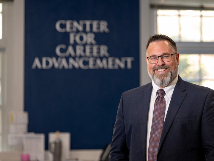 Sean Schofield poses in a suit before a sign that says "Center for Career Advancement"