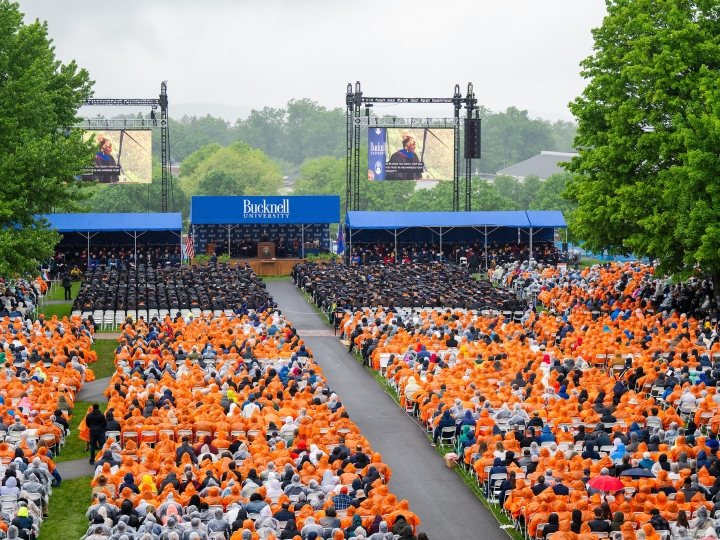 Rows of seniors sit facing the Commencement platform, many dressed in orange ponchos due to rain, at the 2024 Commencement.