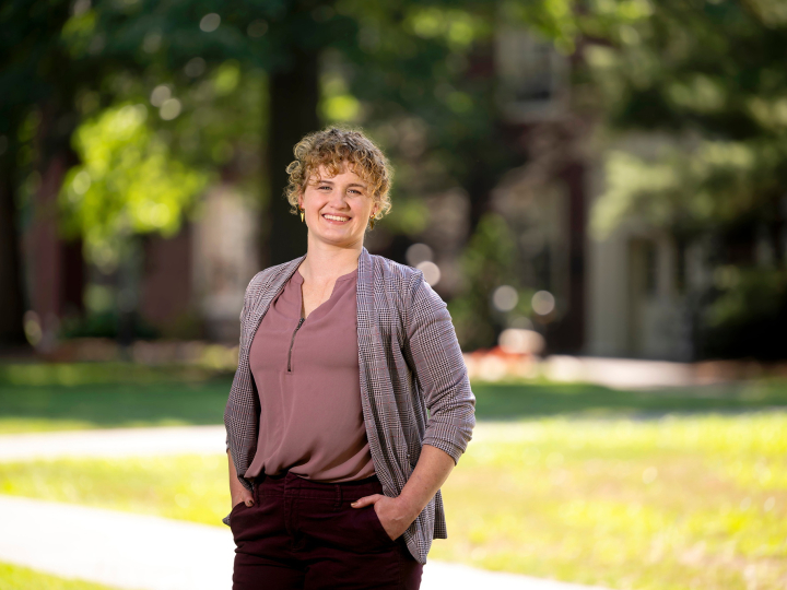 Annie Ross smiles with her hands in her pockets with greenery in the background.