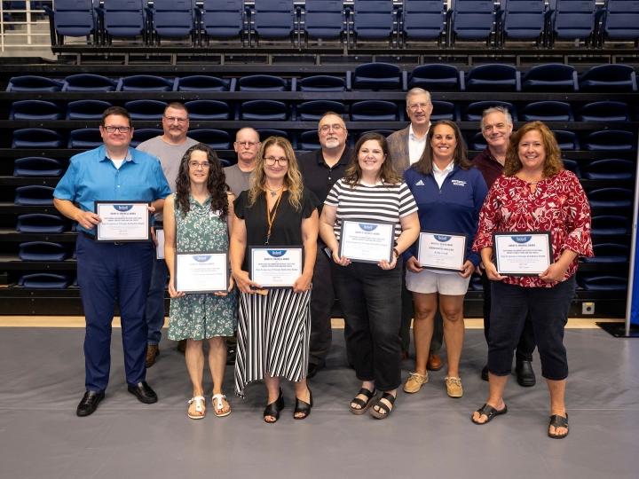 10 employees stand with John Bravman and smile while holding awards