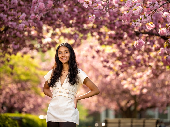 Gabby Diaz '25, in a white dress, poses with her hands on her hips in front of cherry blossom trees.