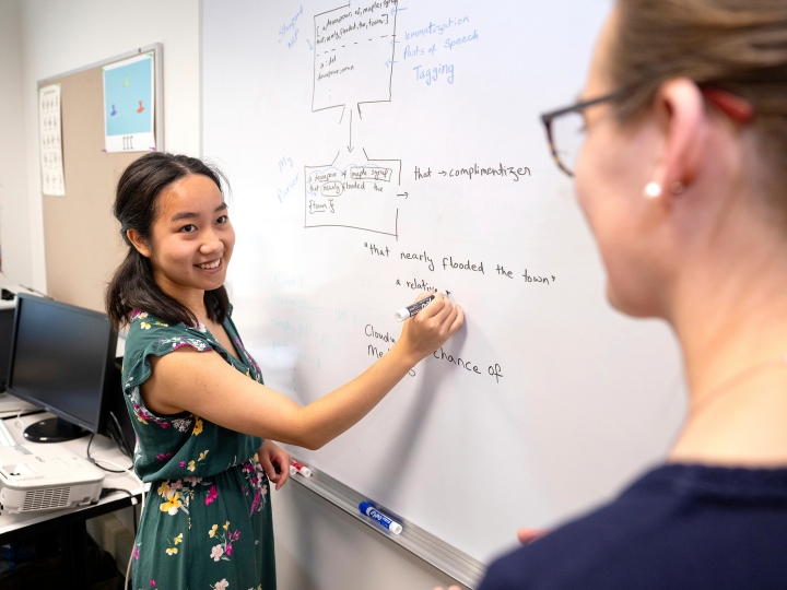Sanda Tan writes on a whiteboard while Professor Heidi Lorimor stands in the foreground.
