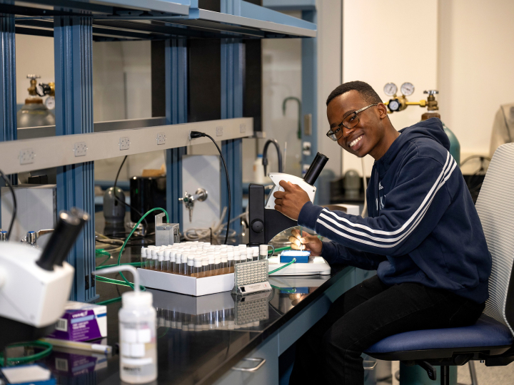 Monwabisi Qeki sits in a chair in a lab setting and smiles as he adjusts a microcope.