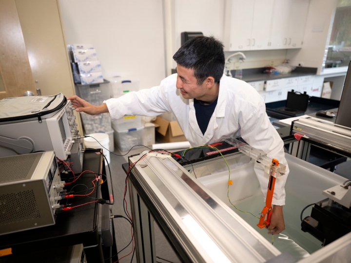 Student Tobey Kim with in a lab wearing a white lab coat and performing a test