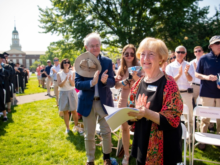 Doris Malesdari S'45 stands and claps and smiles at Commencement, as others in rows behind her also clap and smile.