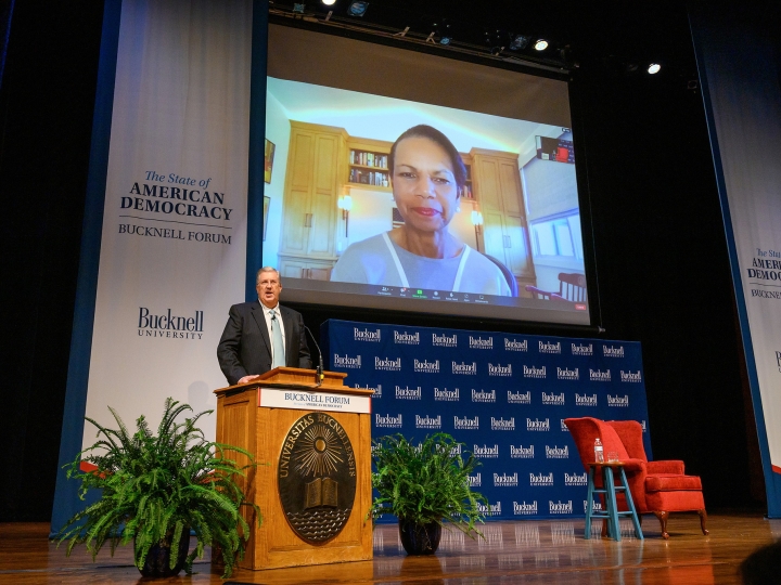 President John Bravman introduces Condoleezza Rice during the Sept. 13 Bucknell Forum event. Bravman stands at a podium with Rice projected on a screen behind him.