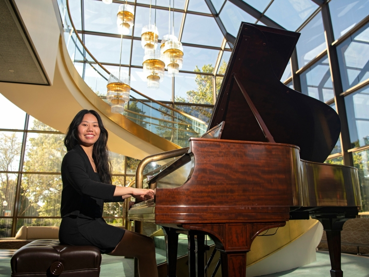 Vivian Kuang sits at a grand piano in a black suit.
