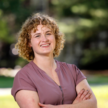 Annie Ross smiles with her arms crossed with greenery in the background.