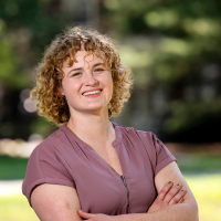 Annie Ross smiles with her arms crossed with greenery in the background.