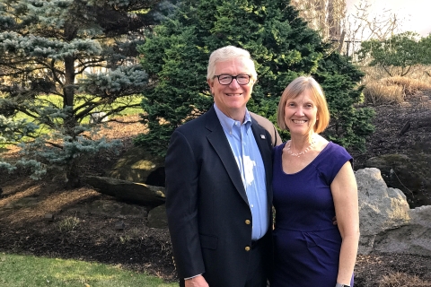 Steve Holmes and his wife, Bonnie Bencsko Holmes &#039;79 pose outside in front of a pine tree