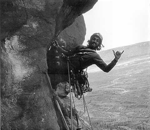 A black and white archival image shows a young man rock climbing on the side of a cliff.
