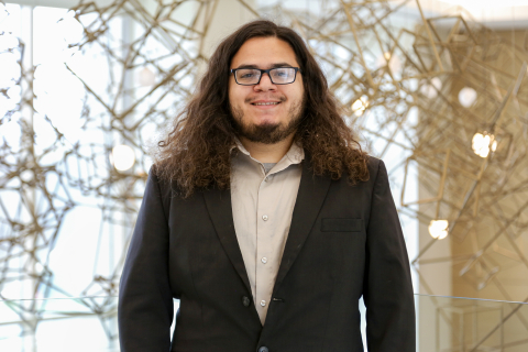 Richard Perez stands and smiles while wearing a dark blazer and beige dress shirt.