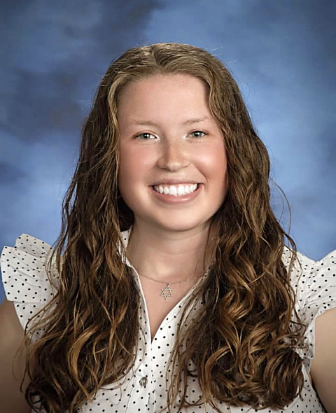 Rebekah Lando wears a white shirt with black dots and smiles against a blue backdrop.