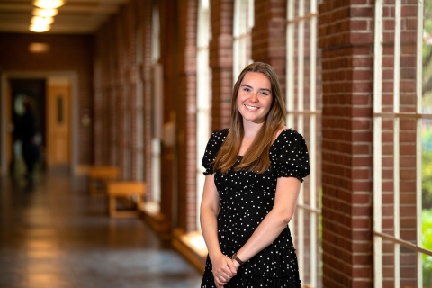 Kendall Robertson stands in a hallway with brick columns and window behind her.