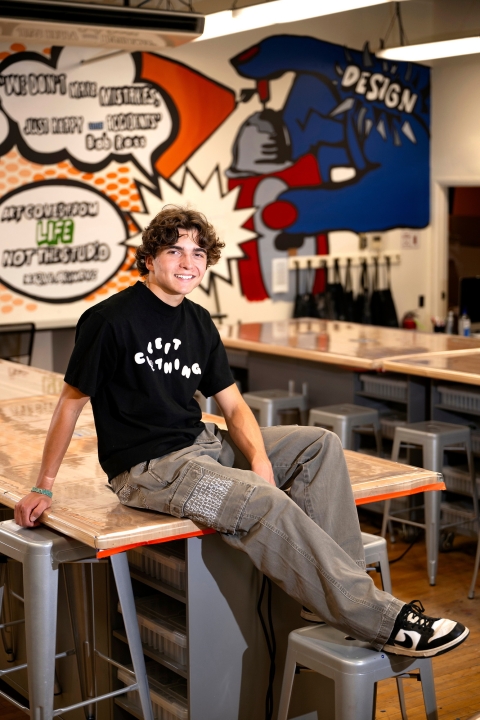Mikey Brandt sits on a table in a colorful Makerspace with a backdrop of graffiti-style art.