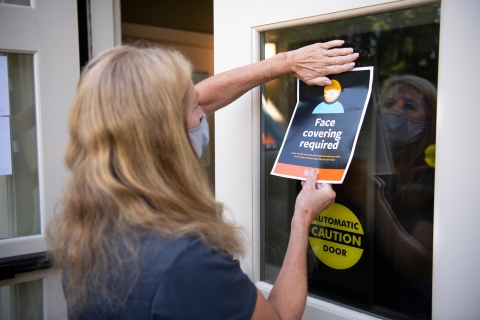 A library worker posts a sign on a door reminding visitors to wear face coverings.