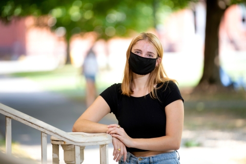 Ella wears a mask and stands on campus