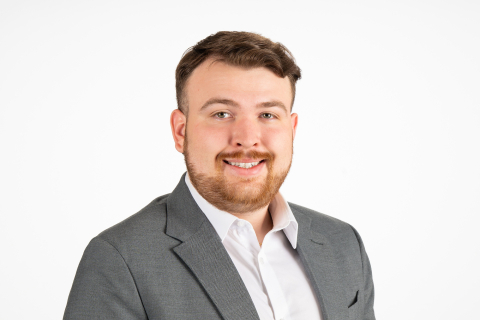 Shane Coudriet wears a white shirt and a gray blazer and smiles against a white backdrop