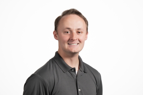Colton Jiorle '25 wears a gray collared shirt and smiles against a white backdrop.
