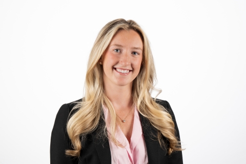 Kaitlyn Trageser '25 wears a pink button-down shirt under a black blazer and smiles against a white backdrop.