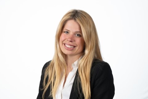 Maddy Davis '25 wears a white button-down collared shirt under a black blazer and smiles against a white backdrop.