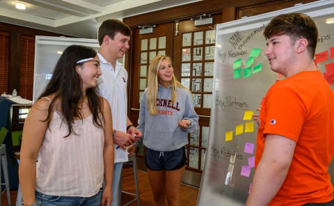 Students gather around a white board with sticky notes on it.